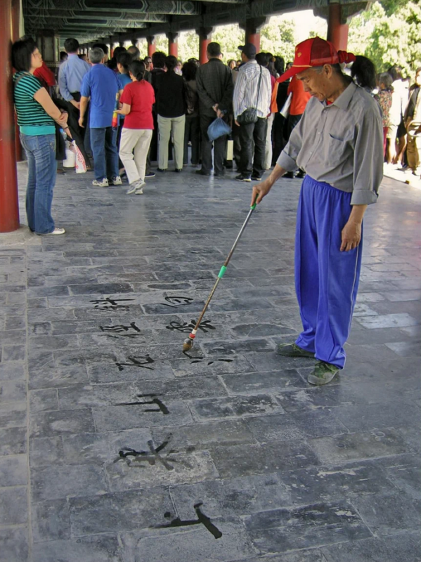 Пожилой китаец пишет иероглифы водой на плитках в галерее в парке Тяньтань (Храм Неба, Пекин)